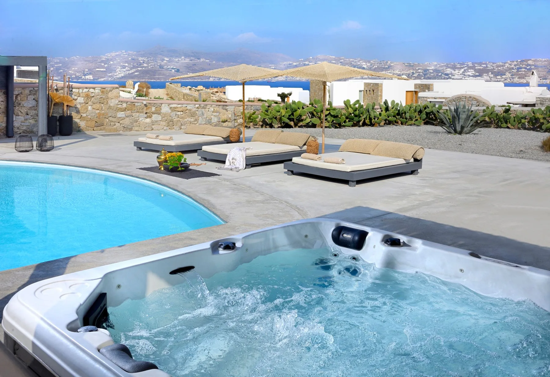 An outdoor pool and hot tub sit beside sun loungers overlooking the coast.