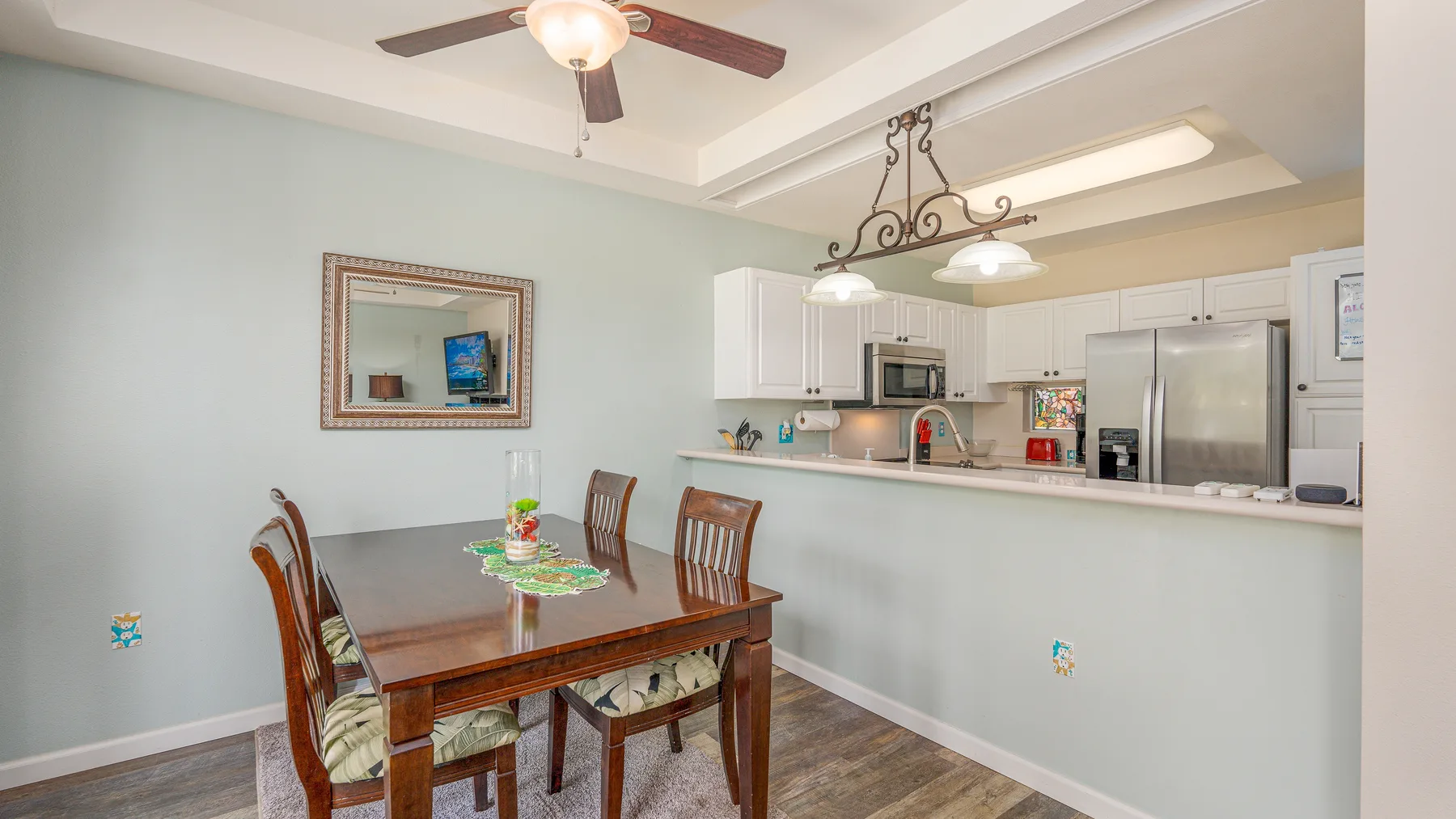 Un comedor se abre a una cocina, con una mesa de madera y luces colgantes.