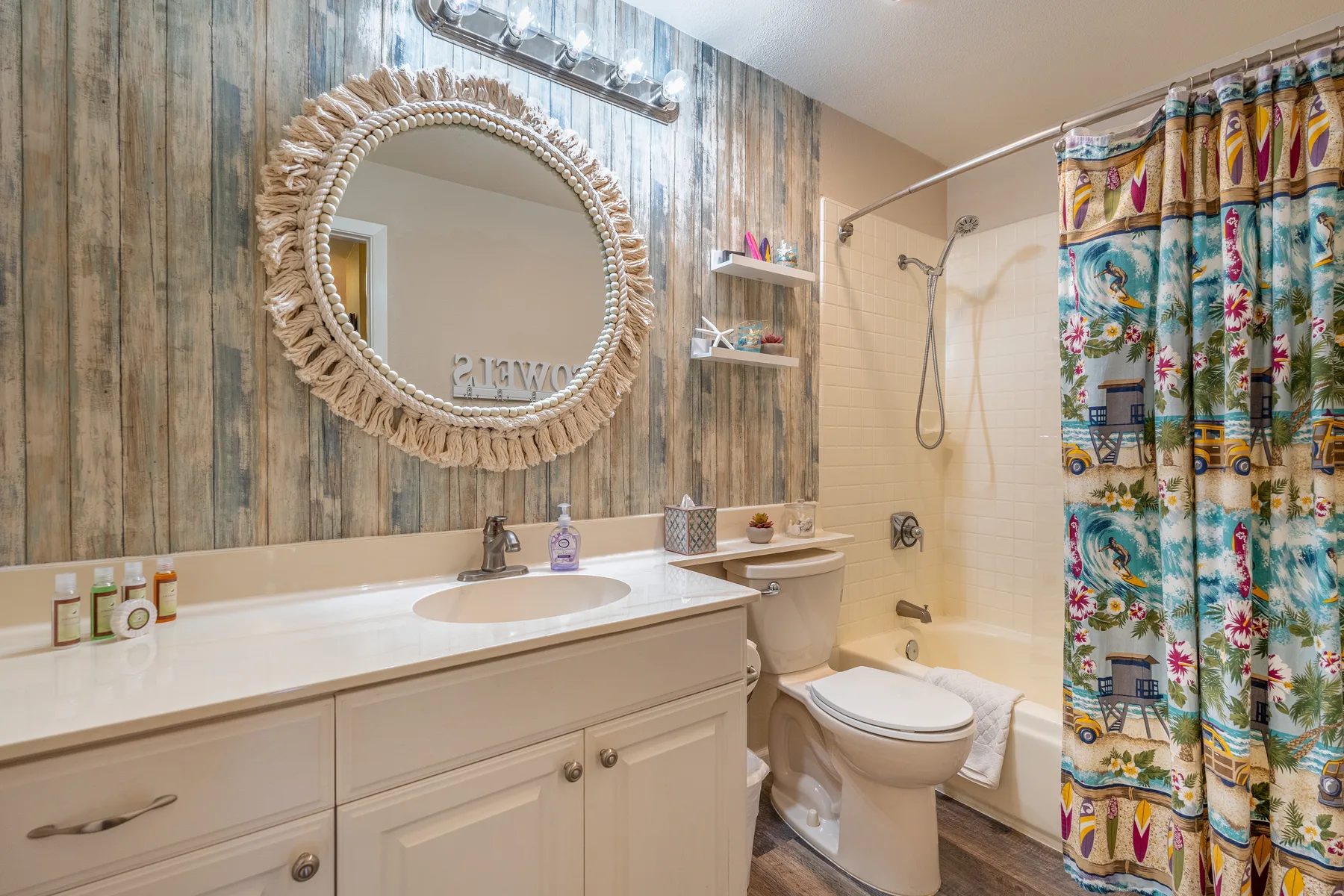 Un baño con lavabo, espejo redondo, inodoro y cortina de ducha colorida.