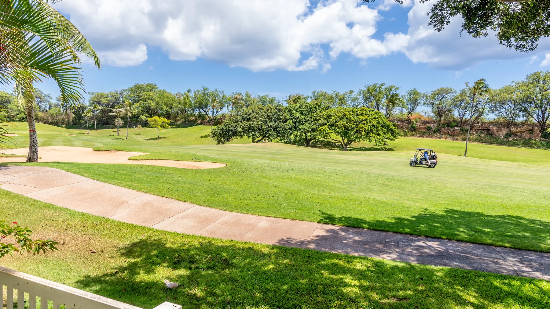 Un amplio campo de golf verde con un camino pavimentado y un carrito de golf pequeño.