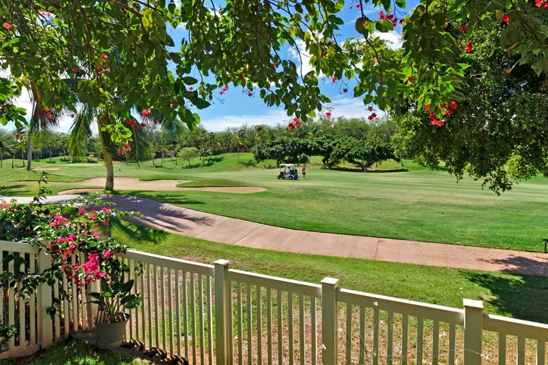 Un campo de golf ajardinado con un sendero pavimentado, árboles y ramas floridas.