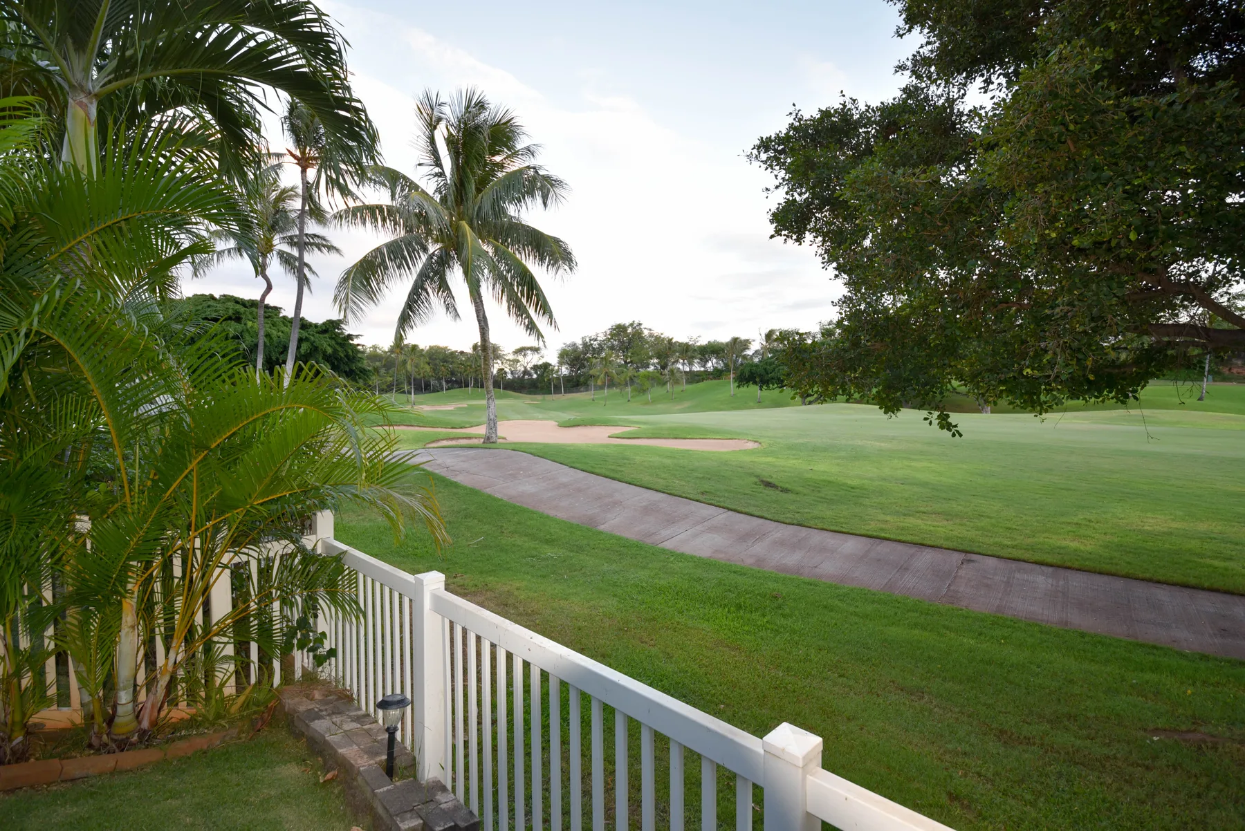 Un campo de golf ajardinado con un camino pavimentado y palmeras.
