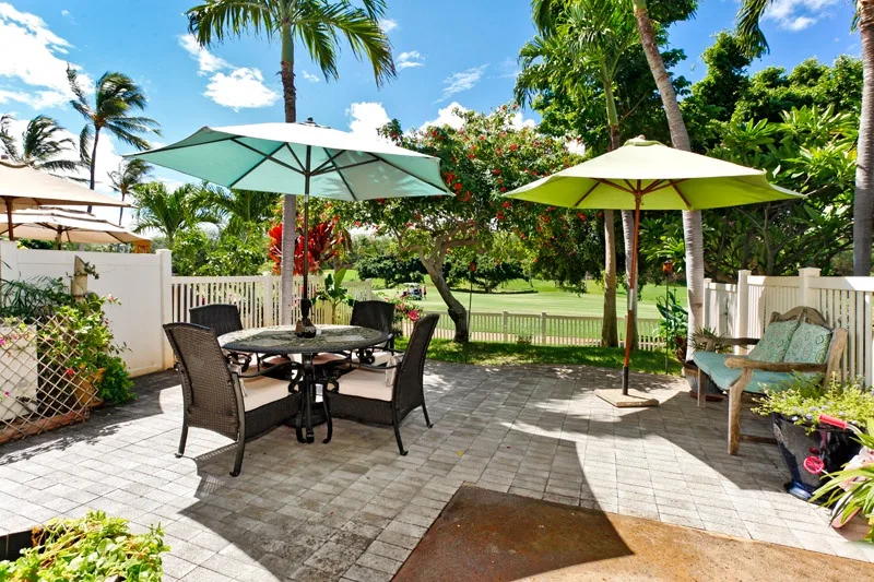 Un patio pavimentado tiene una mesa de comedor, asientos y dos sombrillas grandes.