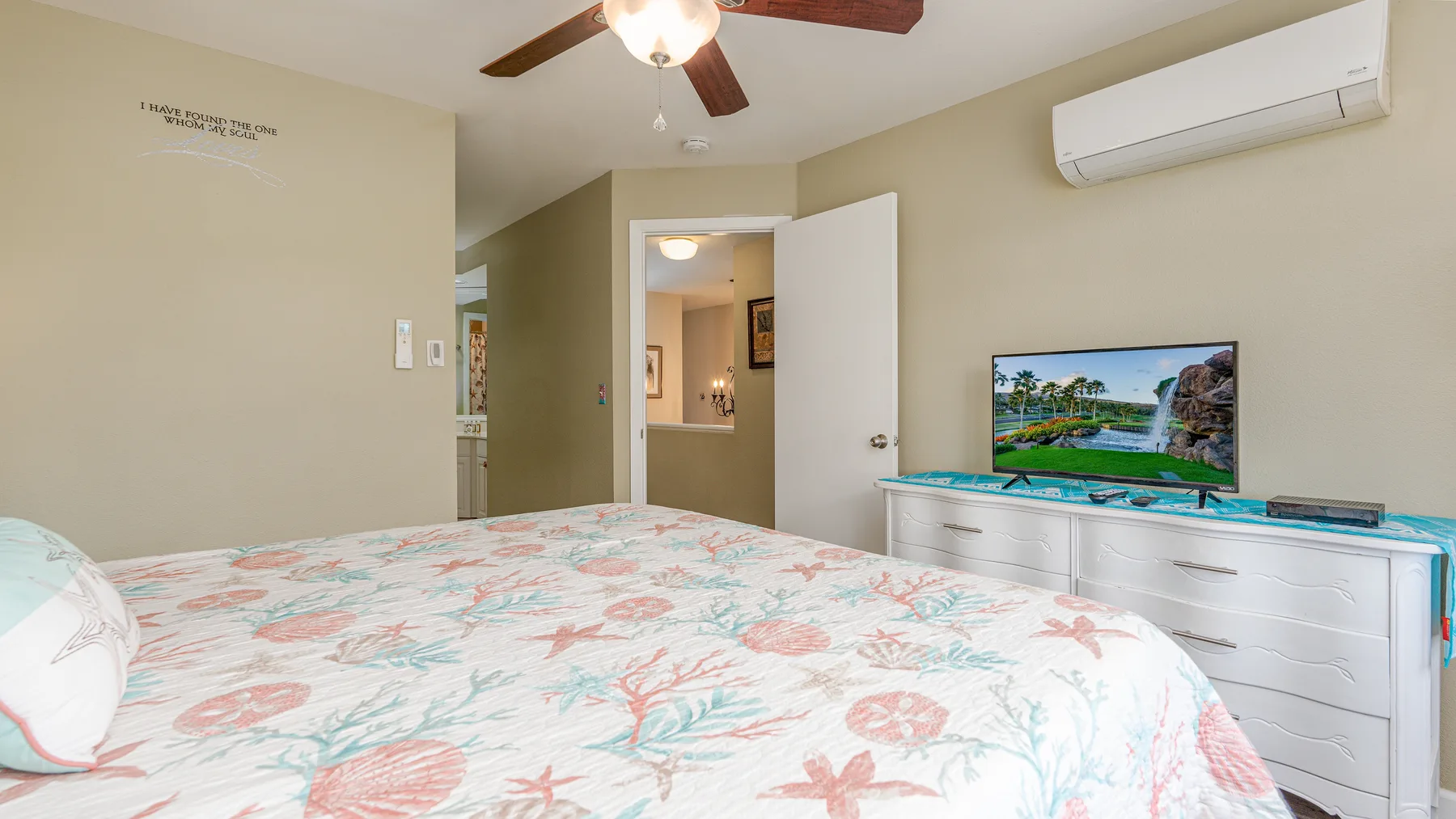 Un dormitorio con una colcha floral, televisor y aire acondicionado en la pared.