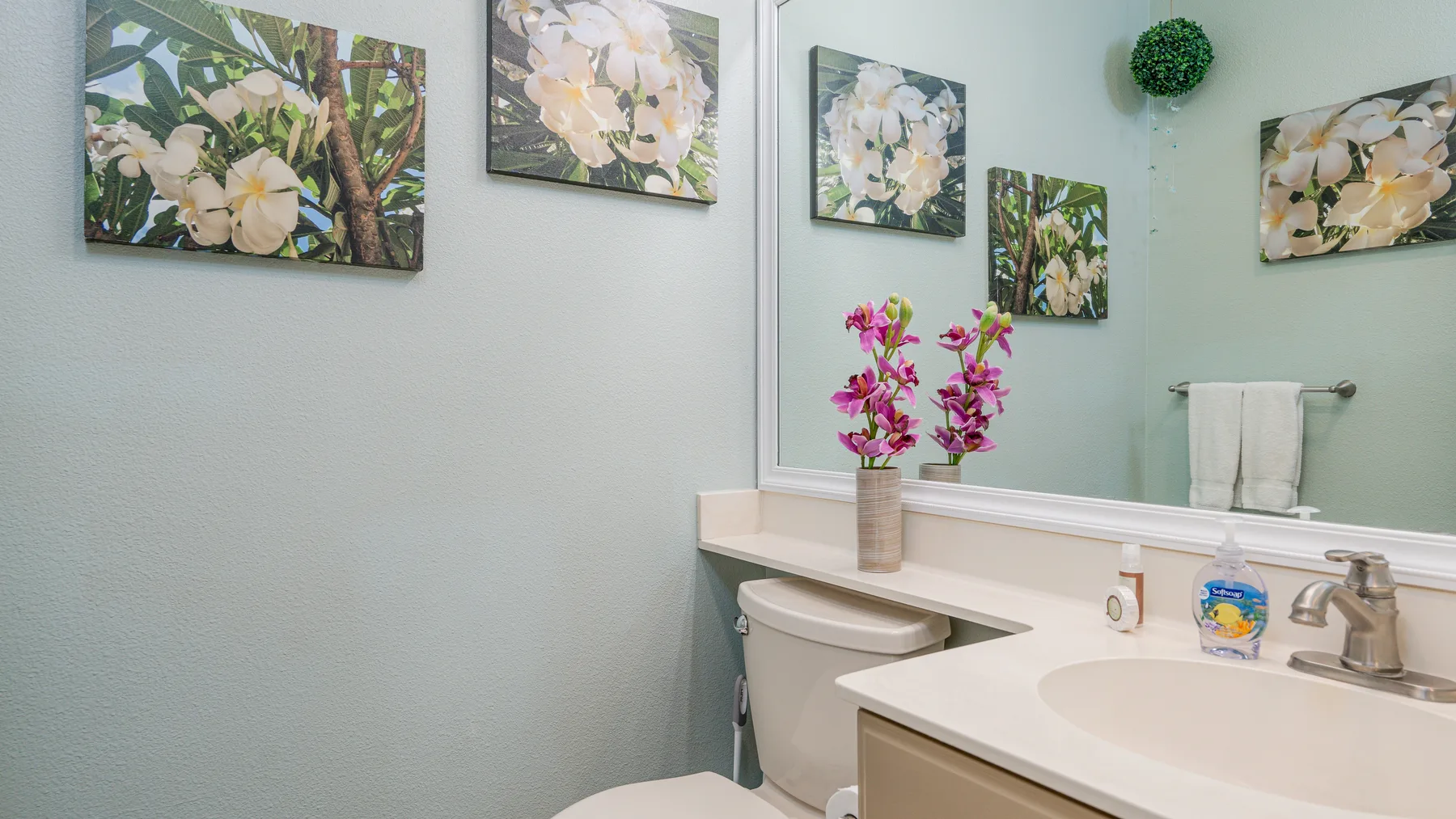 Un tocador de baño con lavabo, espejo y cuadros florales.
