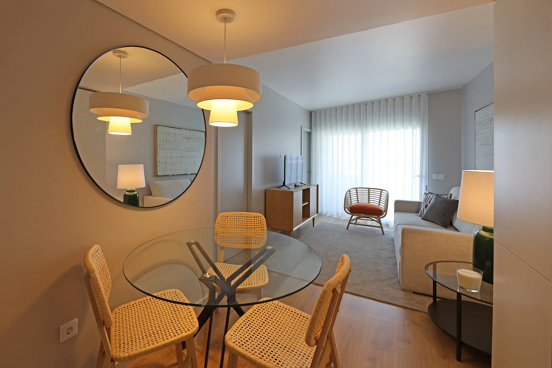 A living room with a glass dining table and seating beside a bright window.