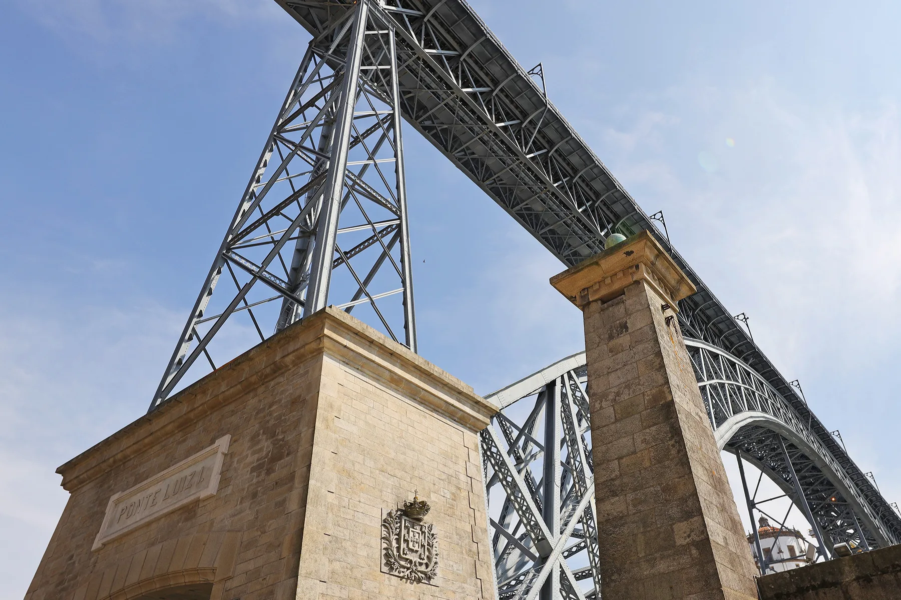 A large steel bridge structure rises above stone support towers against a clear sky.