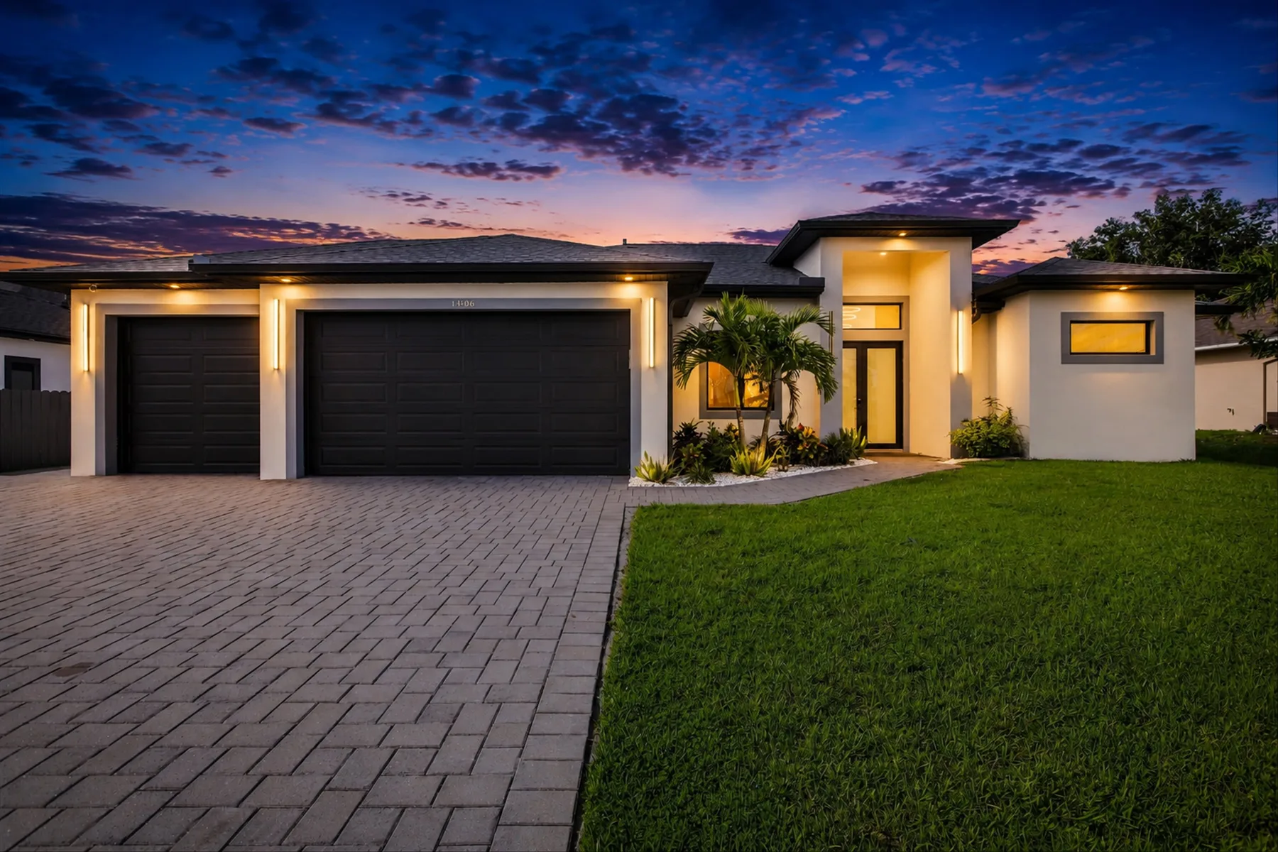 A modern house with a paved driveway and lawn at sunset.