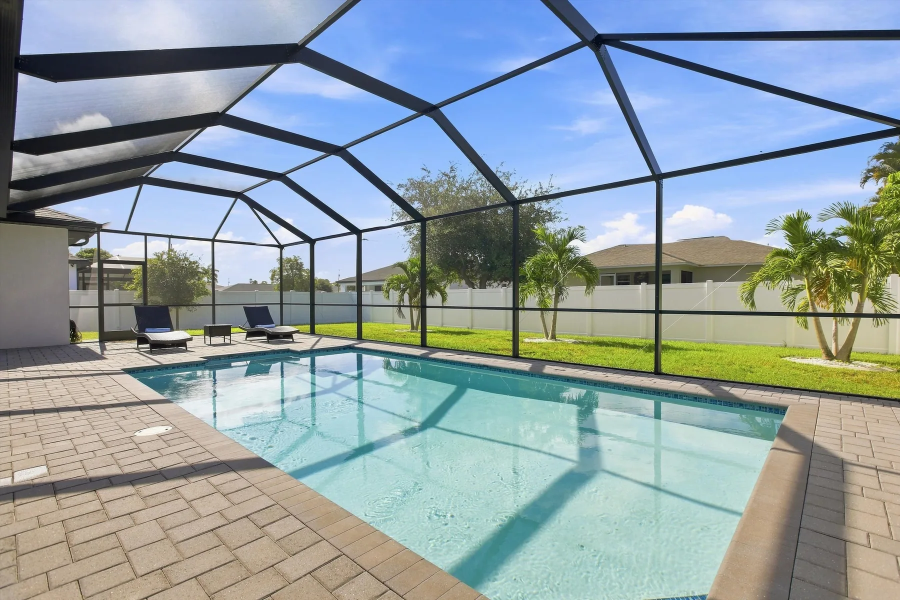 A screened outdoor swimming pool beside a paved patio and lawn.