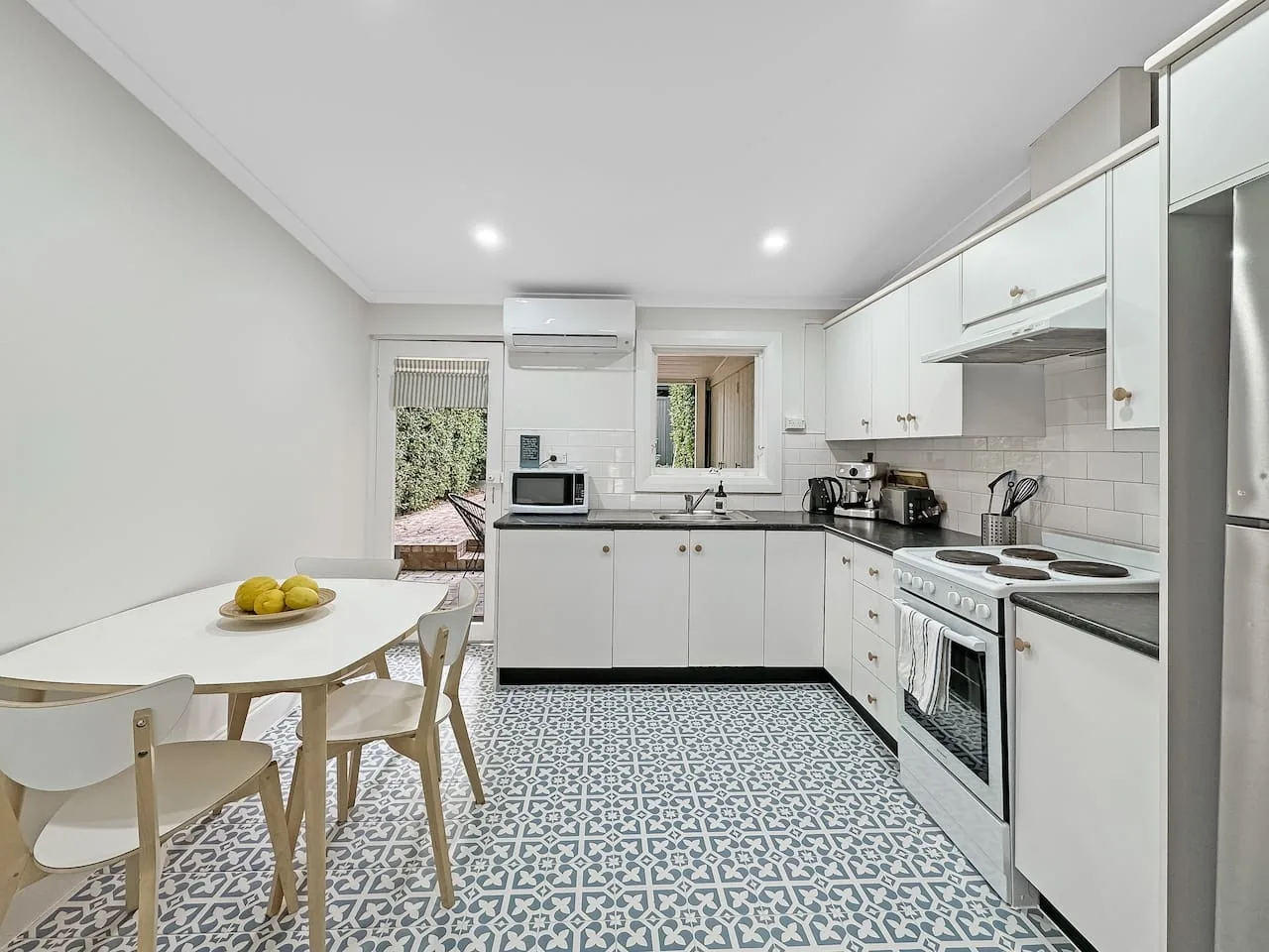 A bright kitchen with white cabinets, a dining table, and patterned tile flooring.