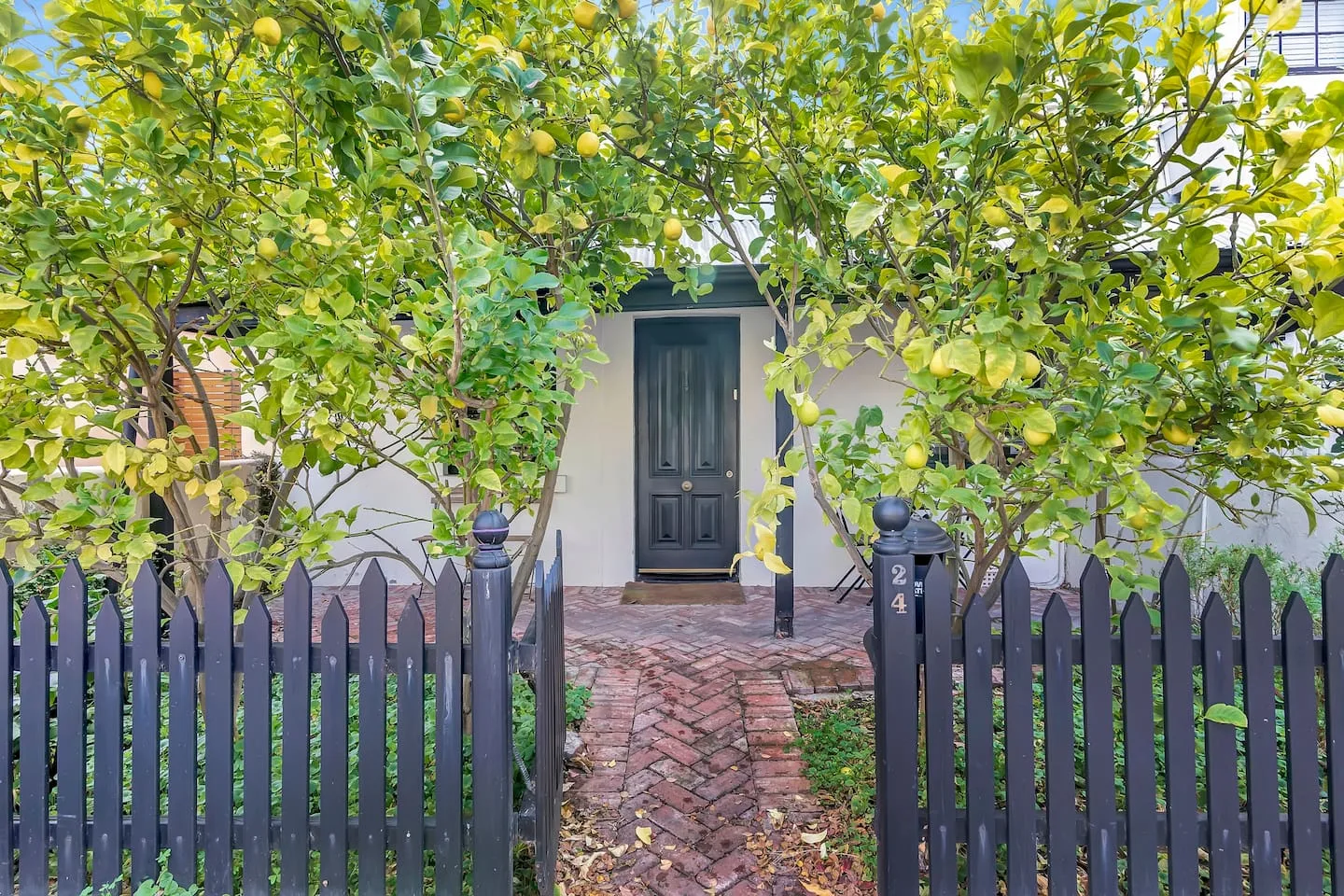 La entrada de una casa de campo queda detrás de una cerca oscura, bajo árboles frondosos.