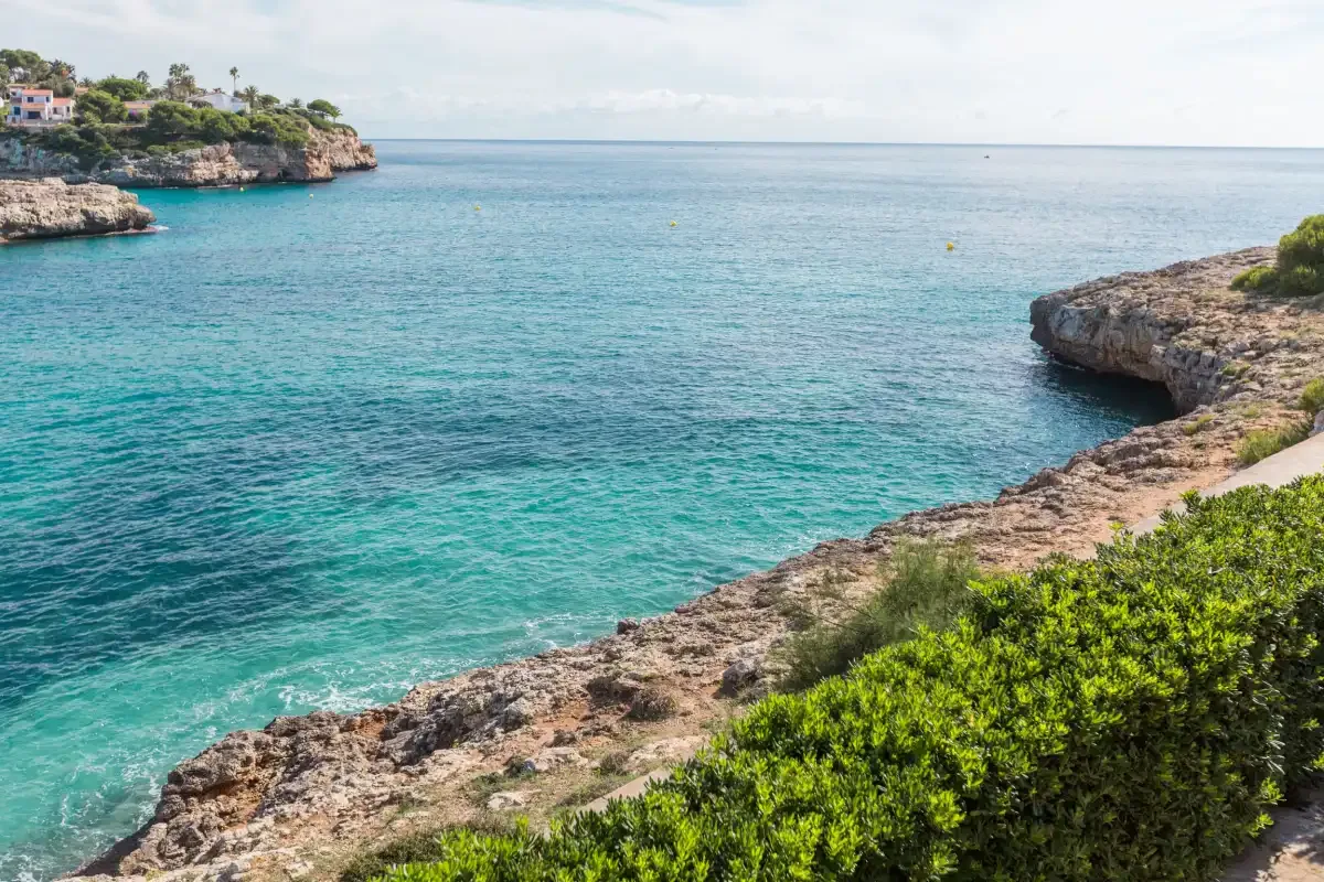 A rocky coastal inlet overlooks clear turquoise water and a distant shoreline.