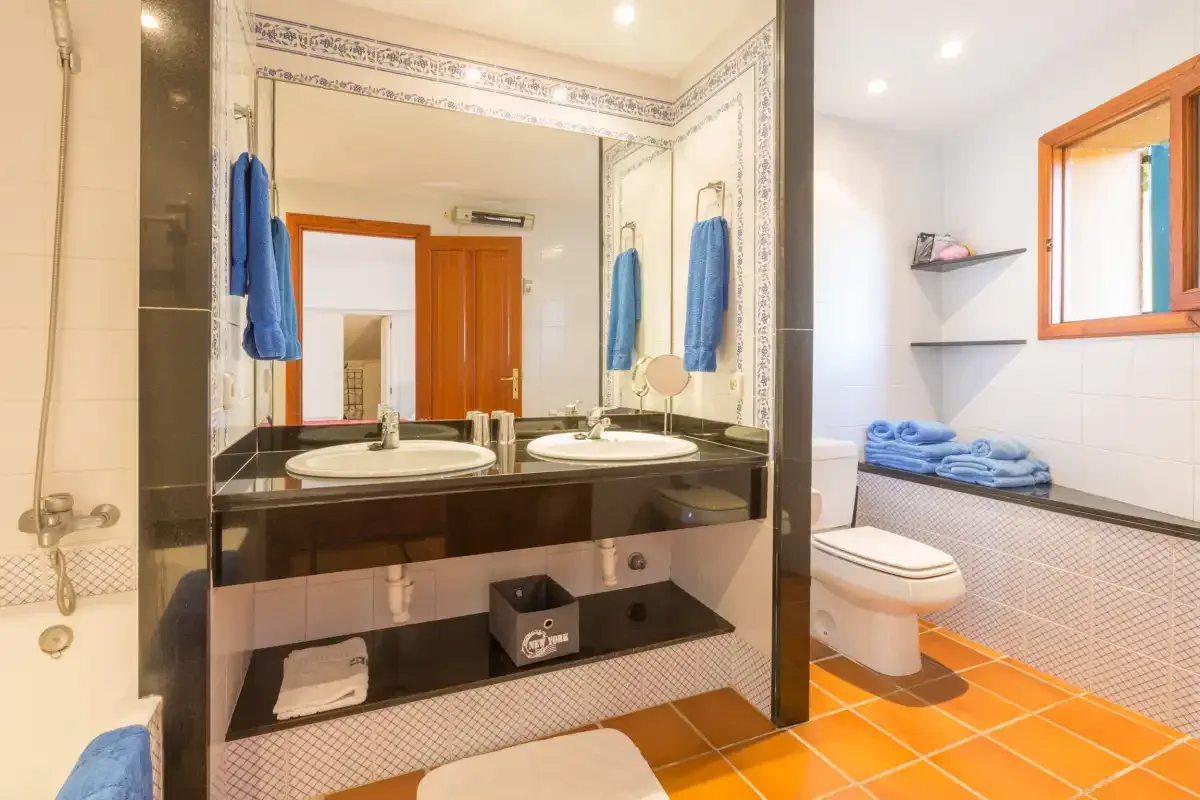 A tiled bathroom has a double-sink vanity, toilet, and window.