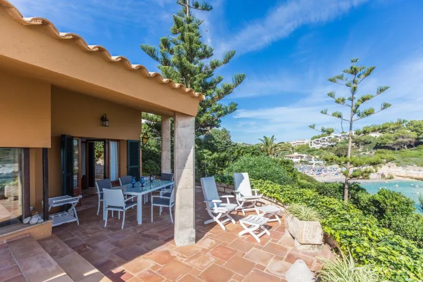 A shaded patio with outdoor seating overlooks greenery and the water.