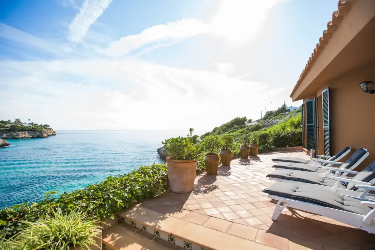 A tiled seaside terrace overlooks the blue water, with loungers beside the building.