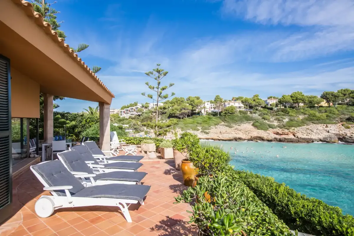 A seaside terrace with lounge seating overlooks a clear turquoise bay.