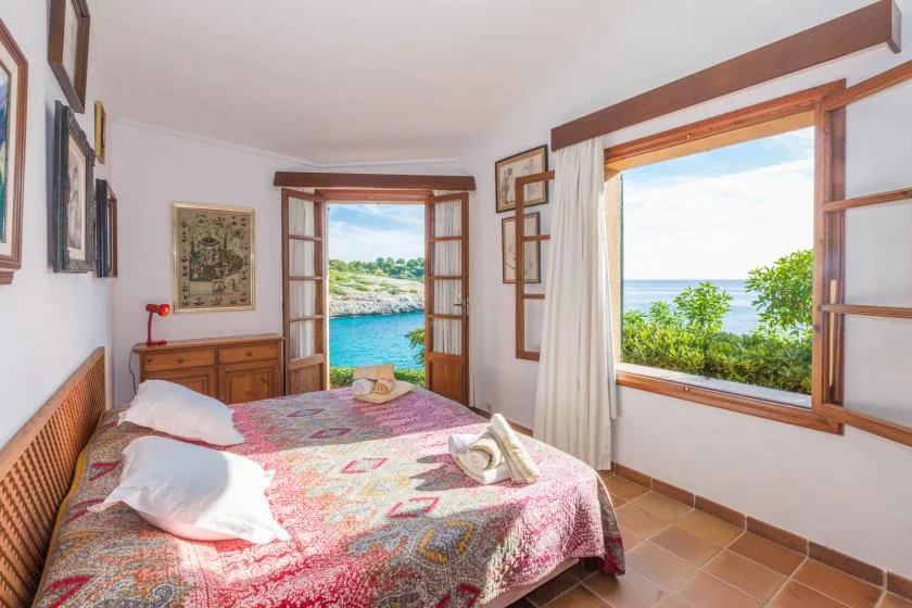 A bedroom with a patterned bedspread and open windows overlooking the sea.