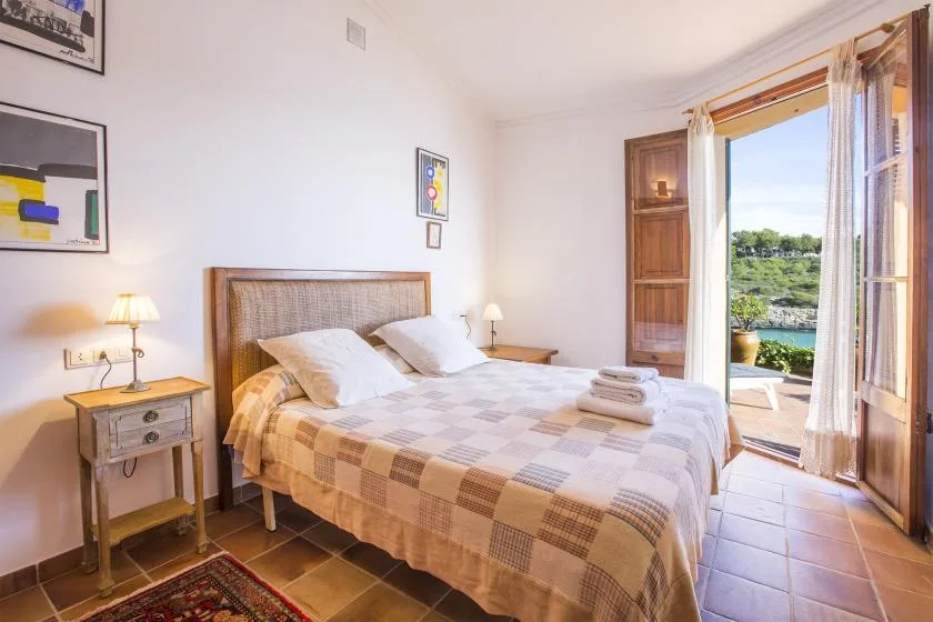 A bedroom with a double bed, bedside tables, and an open door to a balcony.