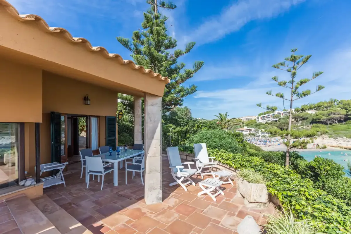 A covered patio with outdoor seating overlooks greenery and the sea.