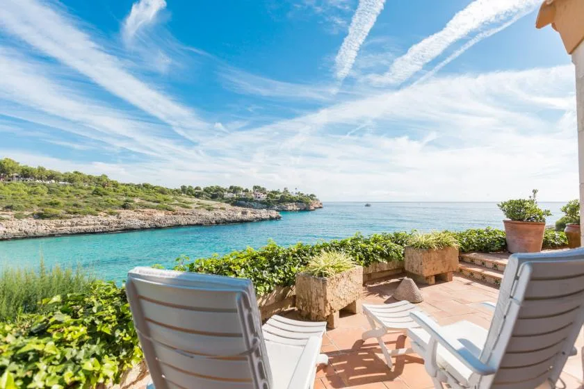 A seaside terrace with seating overlooks a turquoise bay.
