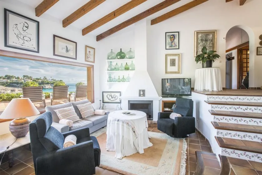 A living room with seating around a draped table and an outdoor view through wide windows.