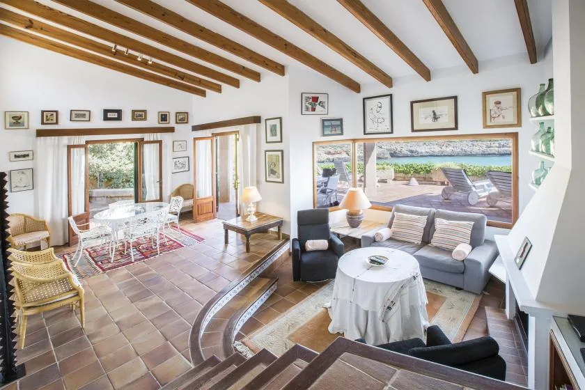 A bright living room opens onto a patio, with seating and exposed wooden ceiling beams.