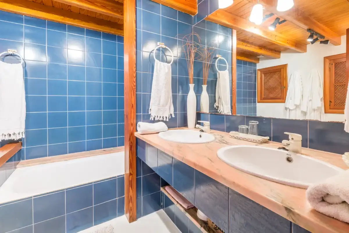 A tiled bathroom with a long vanity, two sinks, and white towels.