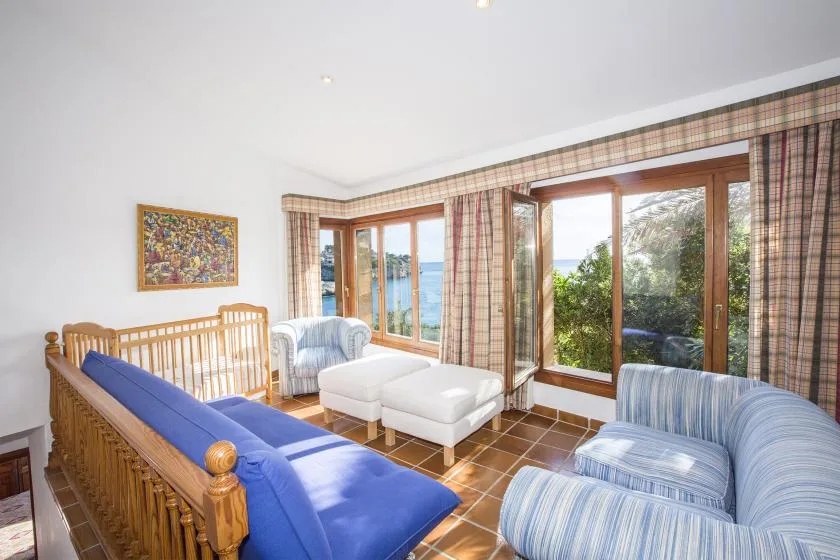 A bright living room with blue seating and large windows overlooking the water.