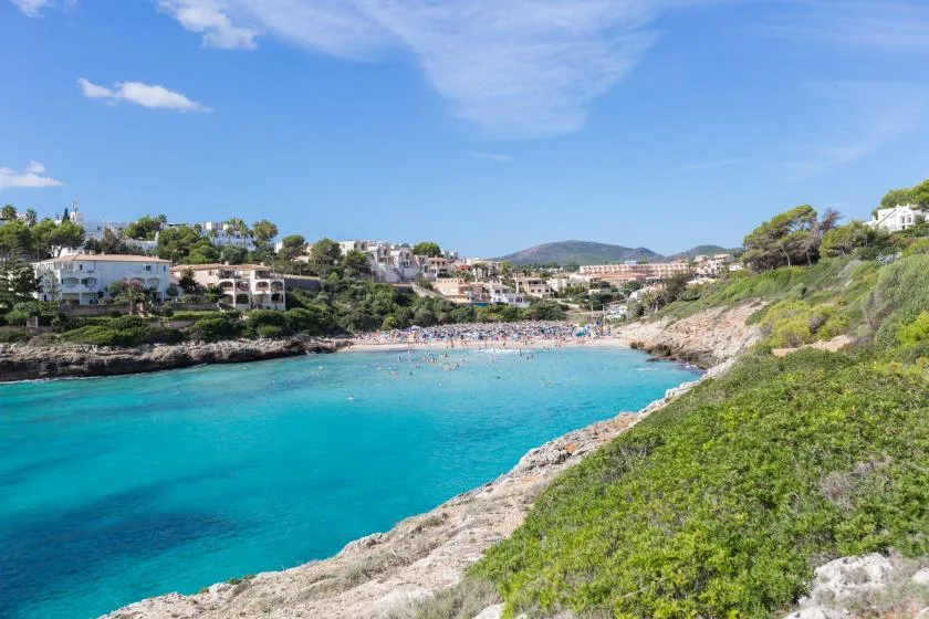 A turquoise bay curves between a rocky shoreline and green coastal slopes.
