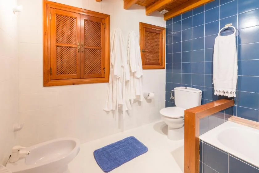 A tiled bathroom with a bathtub, toilet, and blue floor mat.