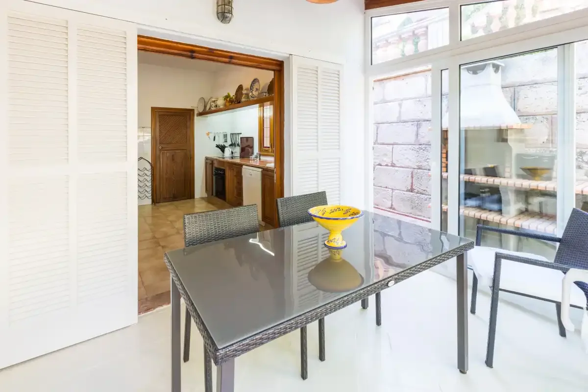 A dining area with a glass table and yellow bowl beside large windows.