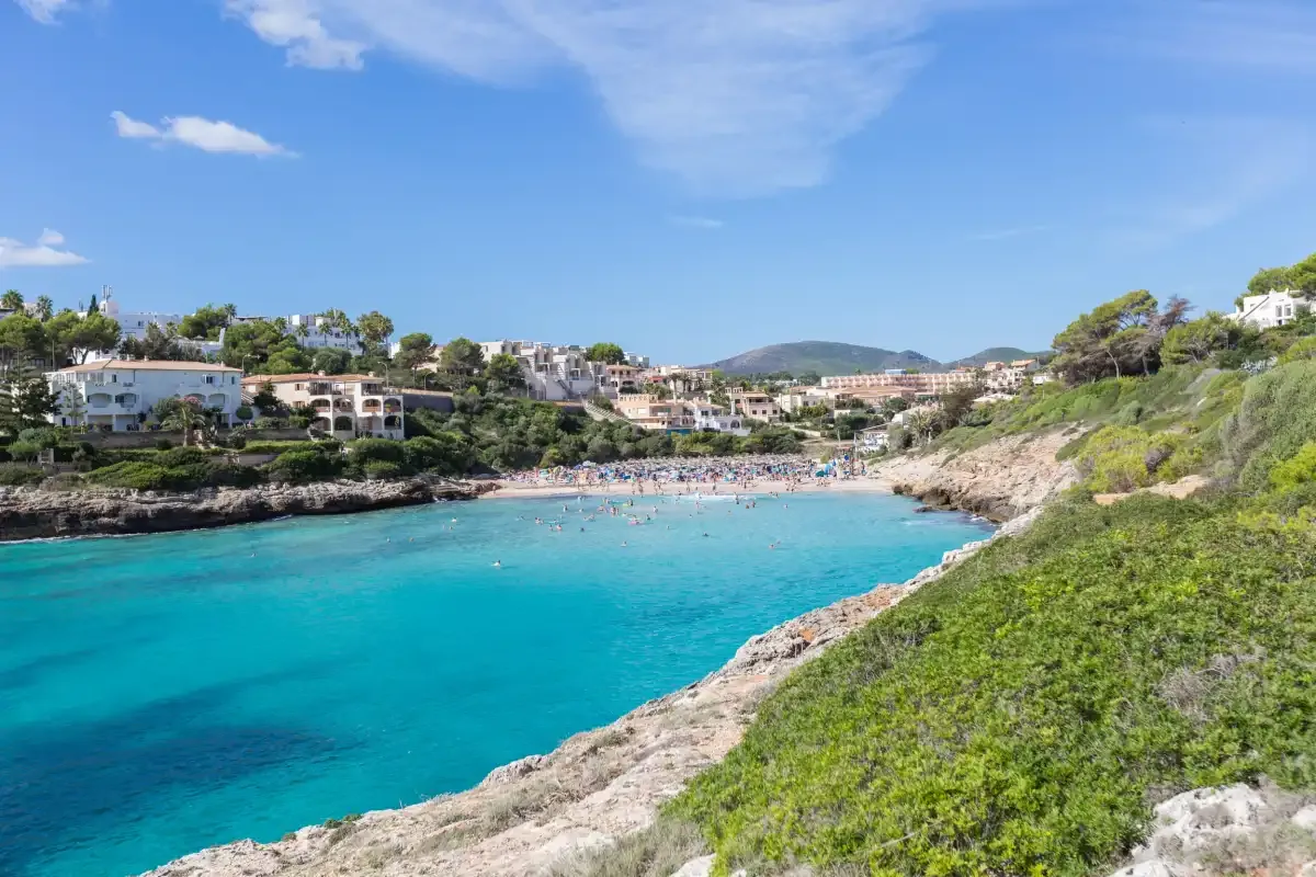 A turquoise coastal bay is bordered by rocky shores and hillside buildings.