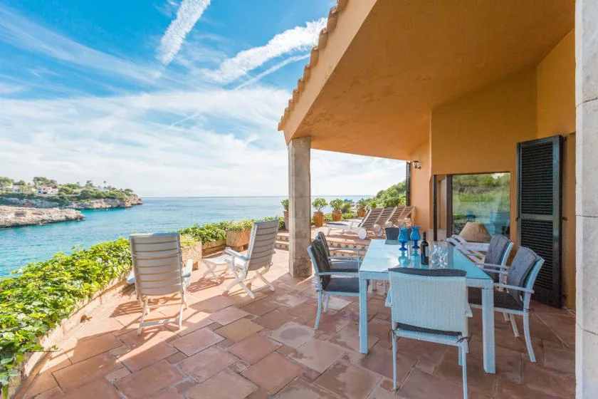 A covered seaside terrace with outdoor seating and a view of the water.