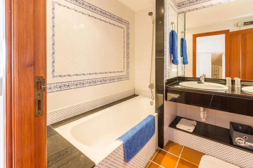 A tiled bathroom with a bathtub, blue towel, and vanity sink.