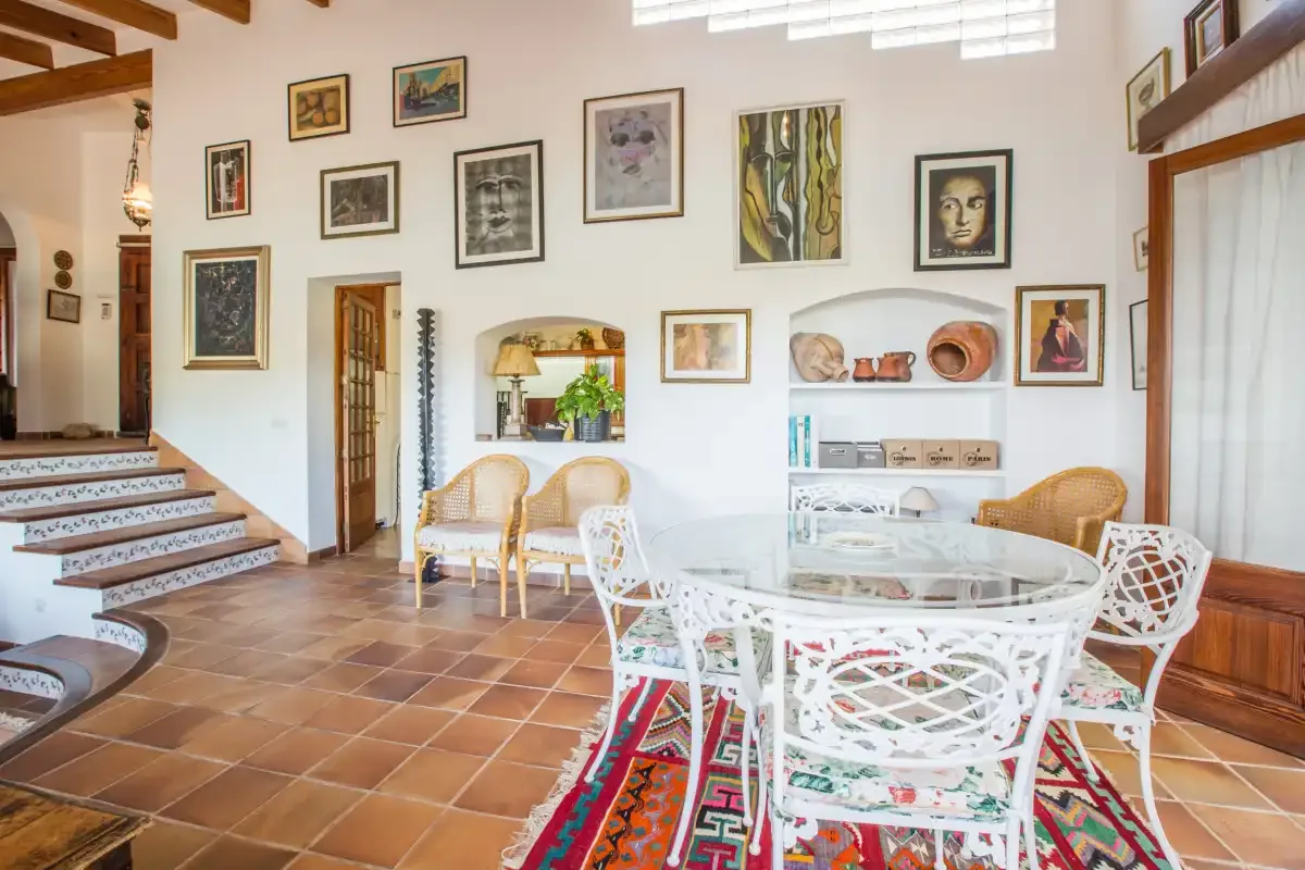 A bright dining area with a glass table, woven seating, and framed artwork.