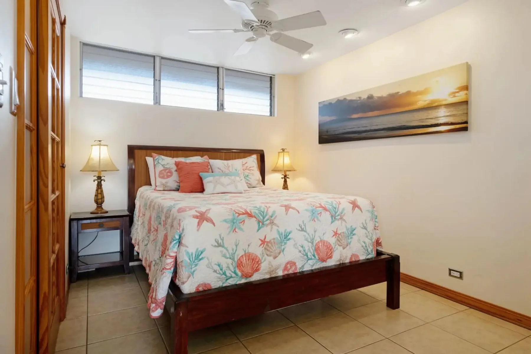 Un dormitorio con una cama cubierta con una colcha floral colorida y lámparas de noche.