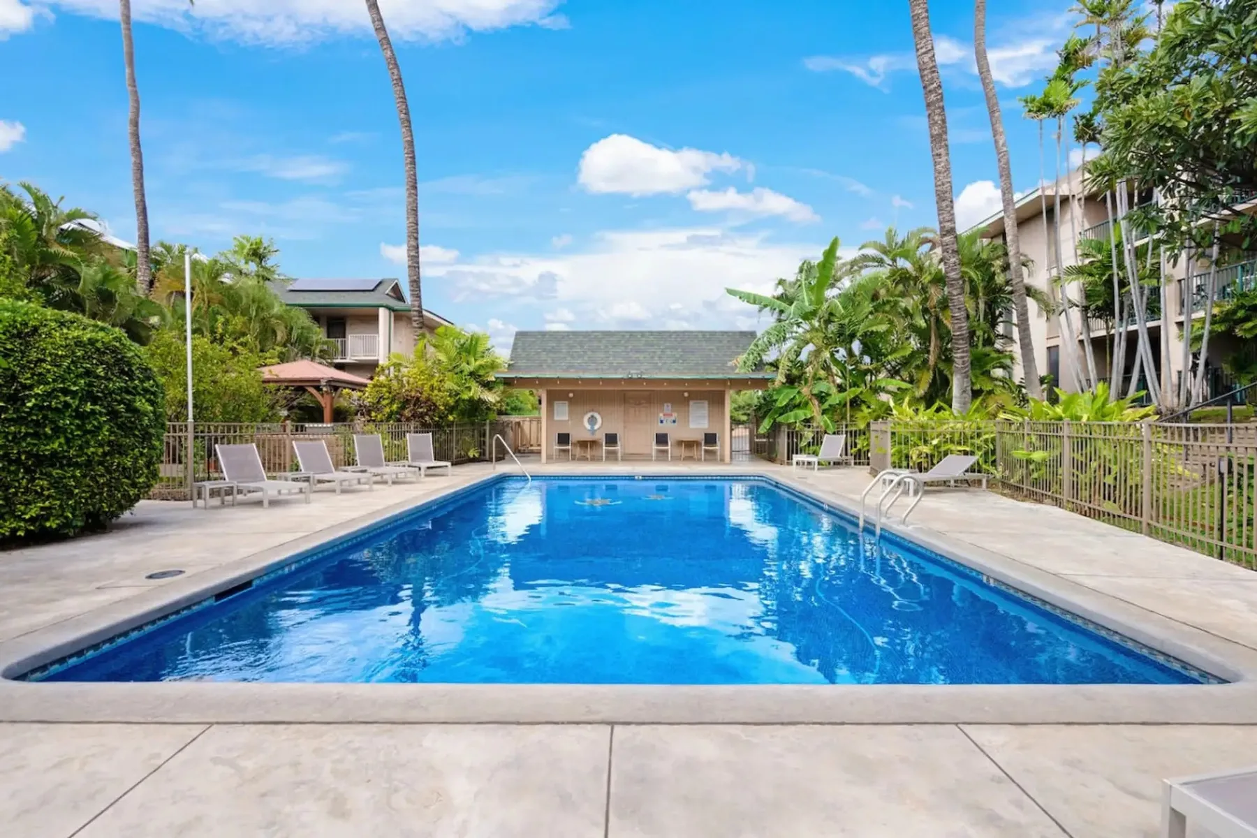 Una piscina exterior luminosa está rodeada de asientos y vegetación tropical.
