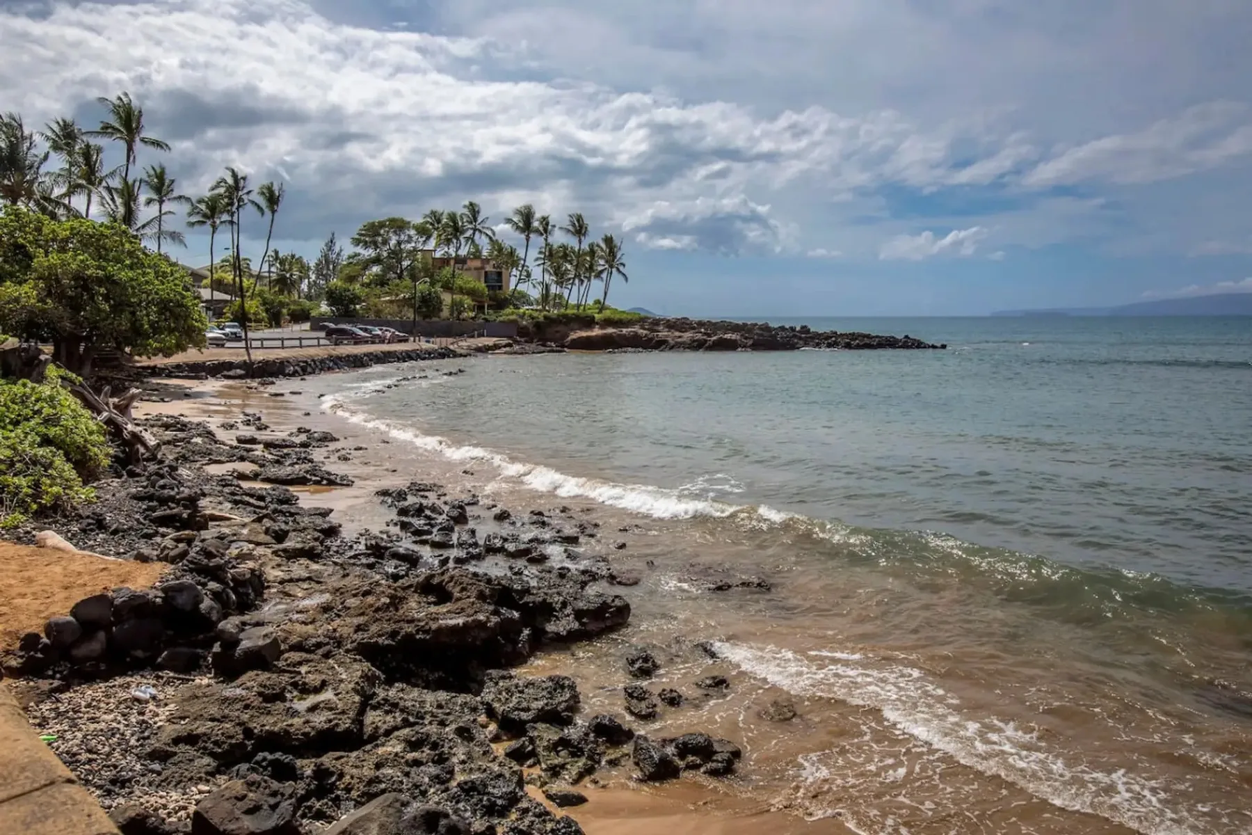 Una costa tropical rocosa bordea una pequeña playa de arena junto a aguas tranquilas.