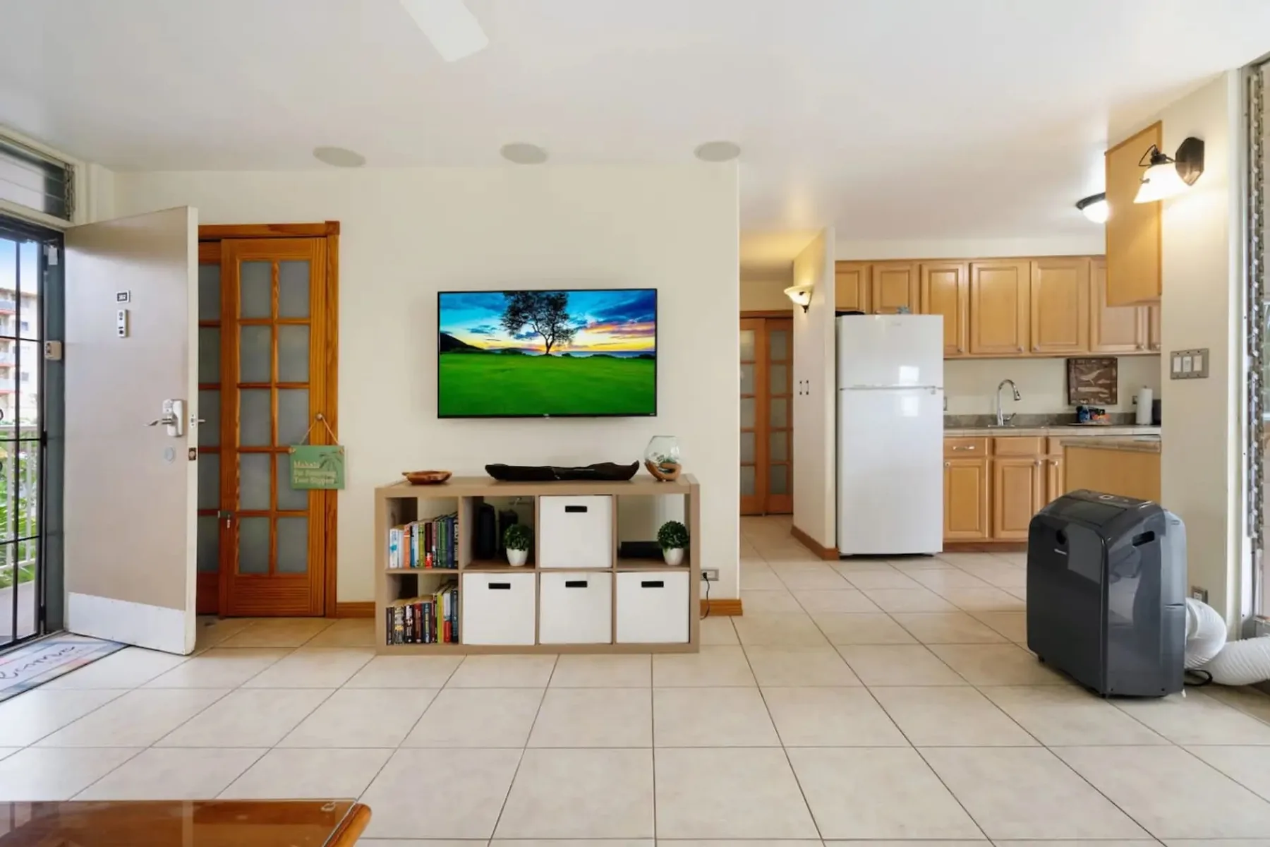Una luminosa sala se abre a una cocina compacta, con un televisor sobre el mueble multimedia.