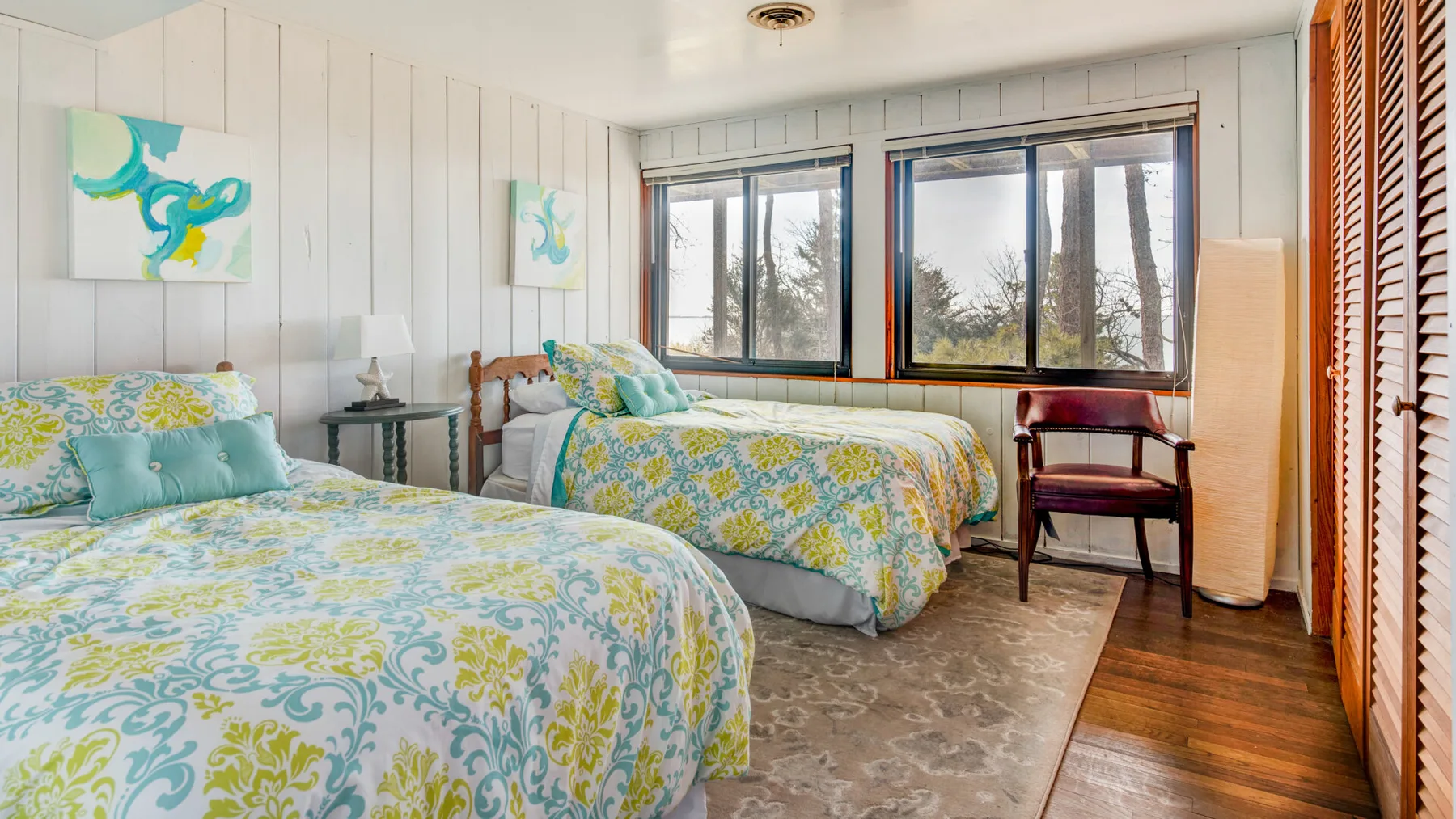Un dormitorio luminoso con dos camas de ropa de cama floral junto a grandes ventanas.