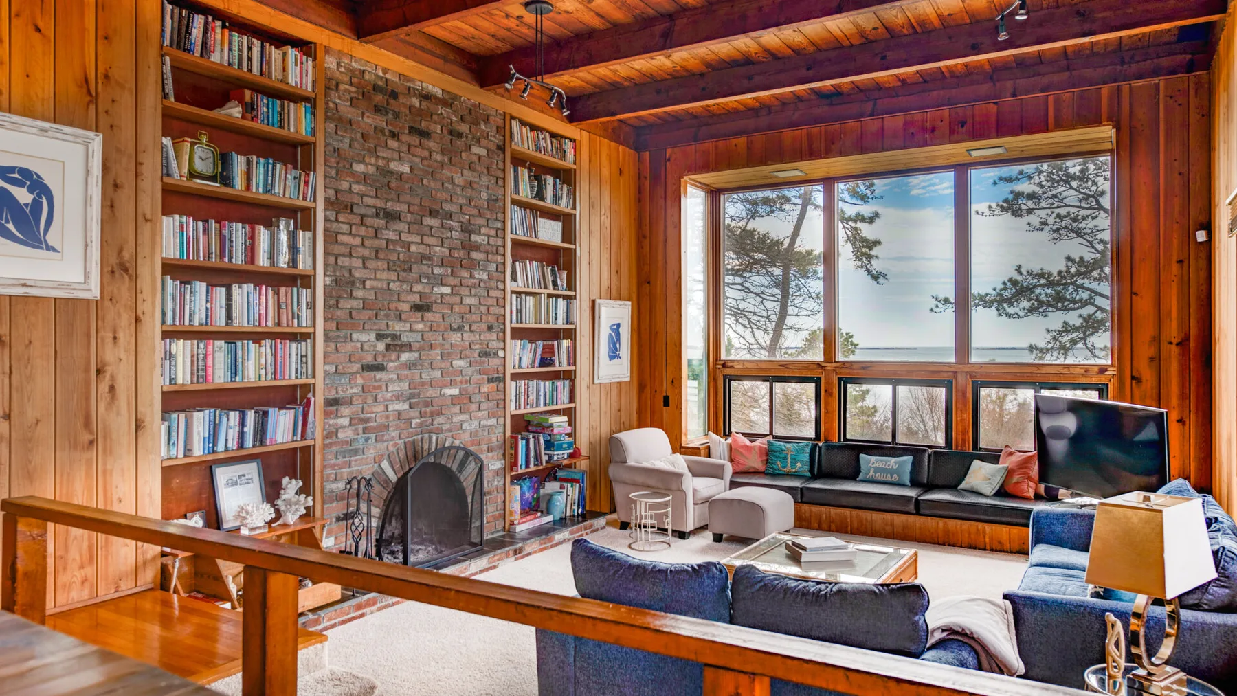 Una sala de estar con paneles de madera, estanterías, una chimenea de ladrillo y una ventana grande.