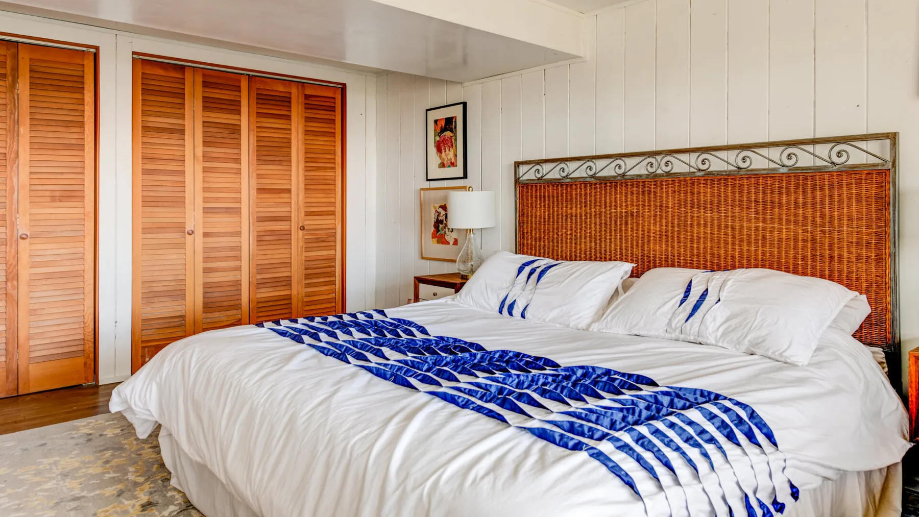 Un dormitorio con una cama grande, ropa de cama blanca y una manta azul estampada.