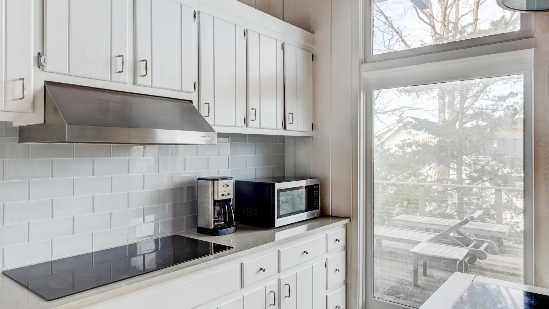 A bright kitchen with white cabinetry, a cooktop, and large windows.