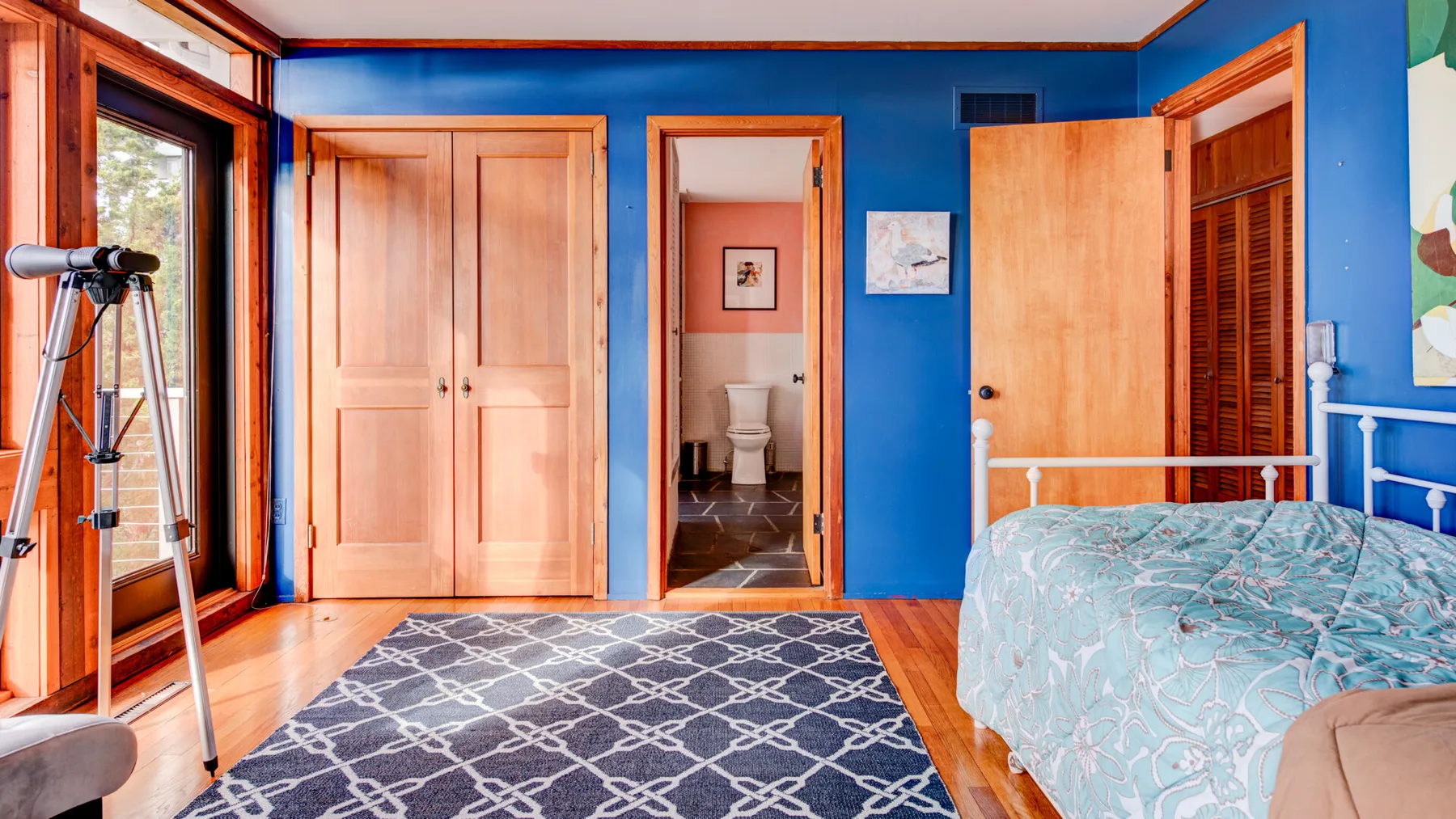 Un dormitorio azul con una alfombra estampada, puertas de madera y una cama.