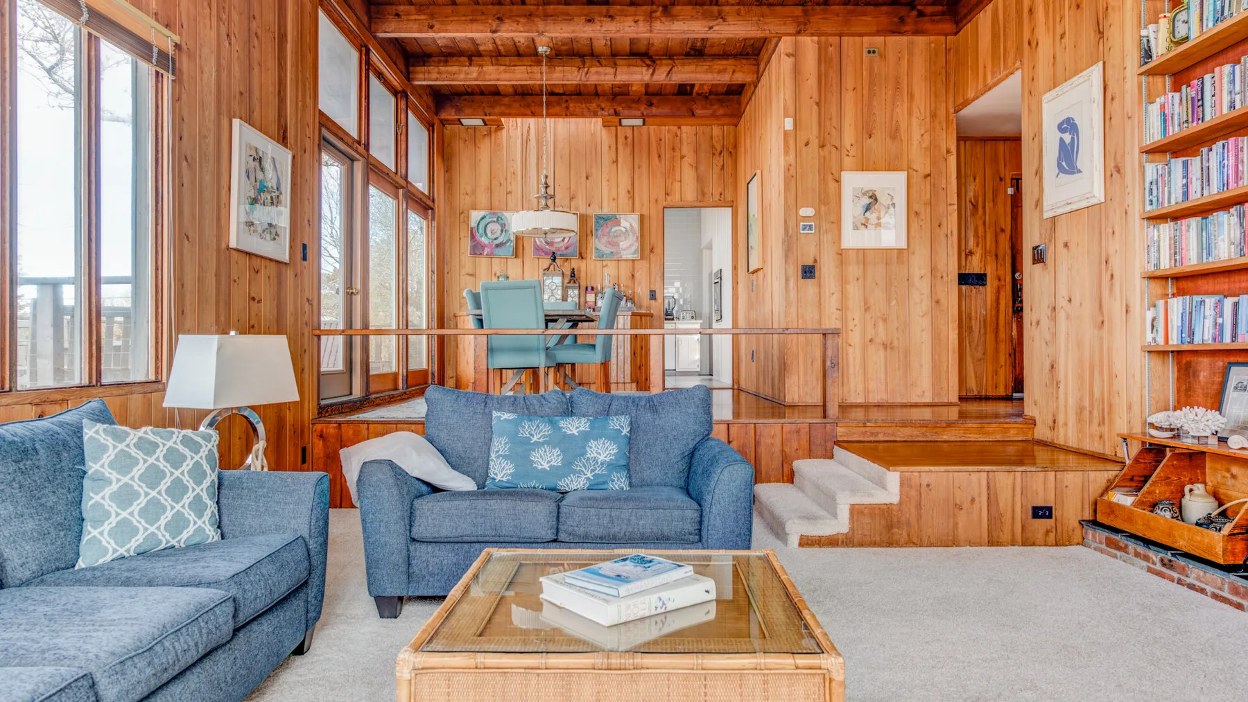 Una sala con paredes de madera, asientos azules y una mesa de centro con tapa de vidrio.