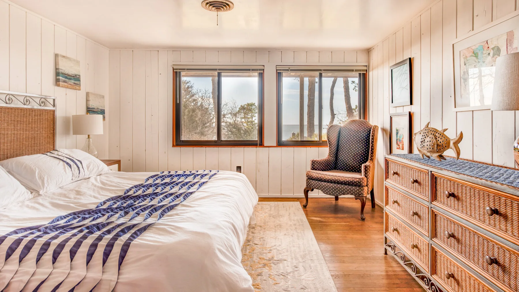 Un dormitorio luminoso con una cama, un sillón y ventanas con vista a los árboles.