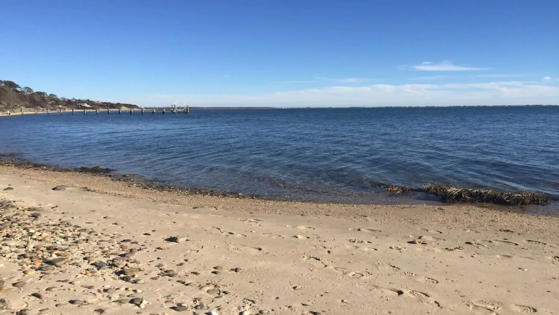 Una playa de arena bordea aguas azules tranquilas bajo un cielo despejado.