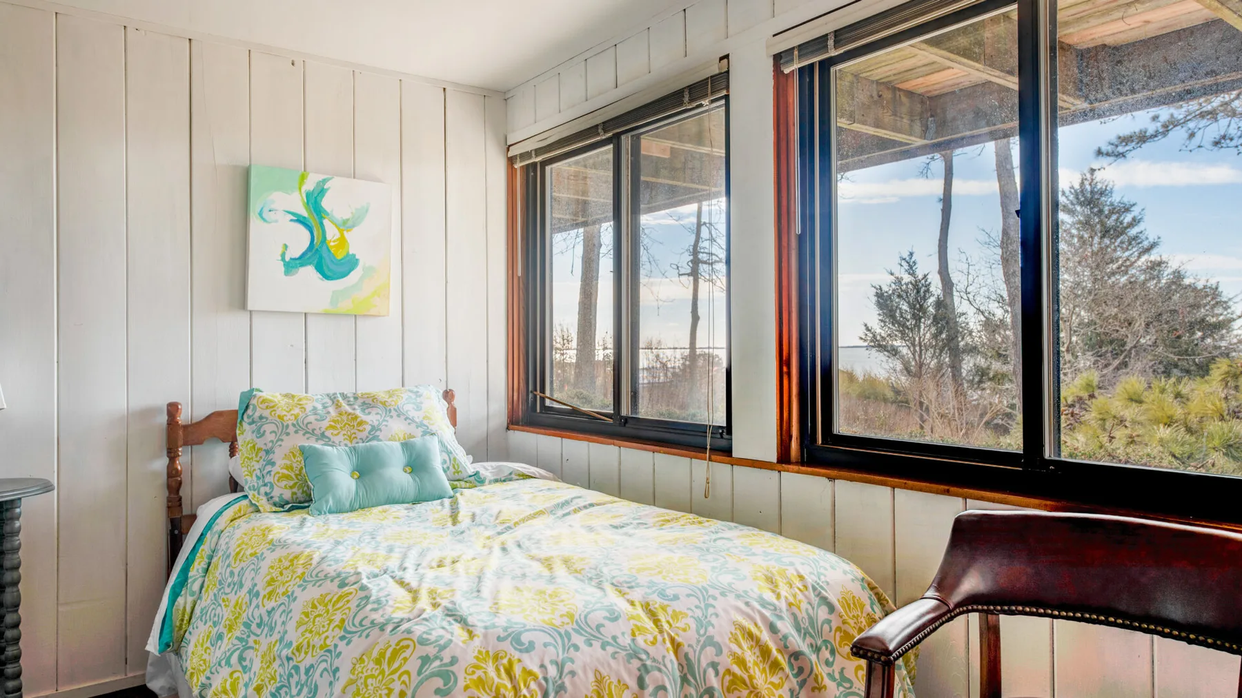 Un dormitorio con una cama junto a grandes ventanas con vistas a árboles.