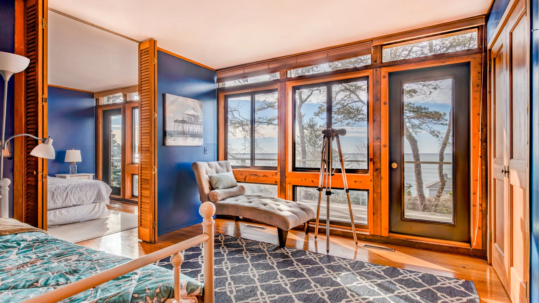 Un dormitorio luminoso con grandes ventanales que dan a un lago y un sillón.