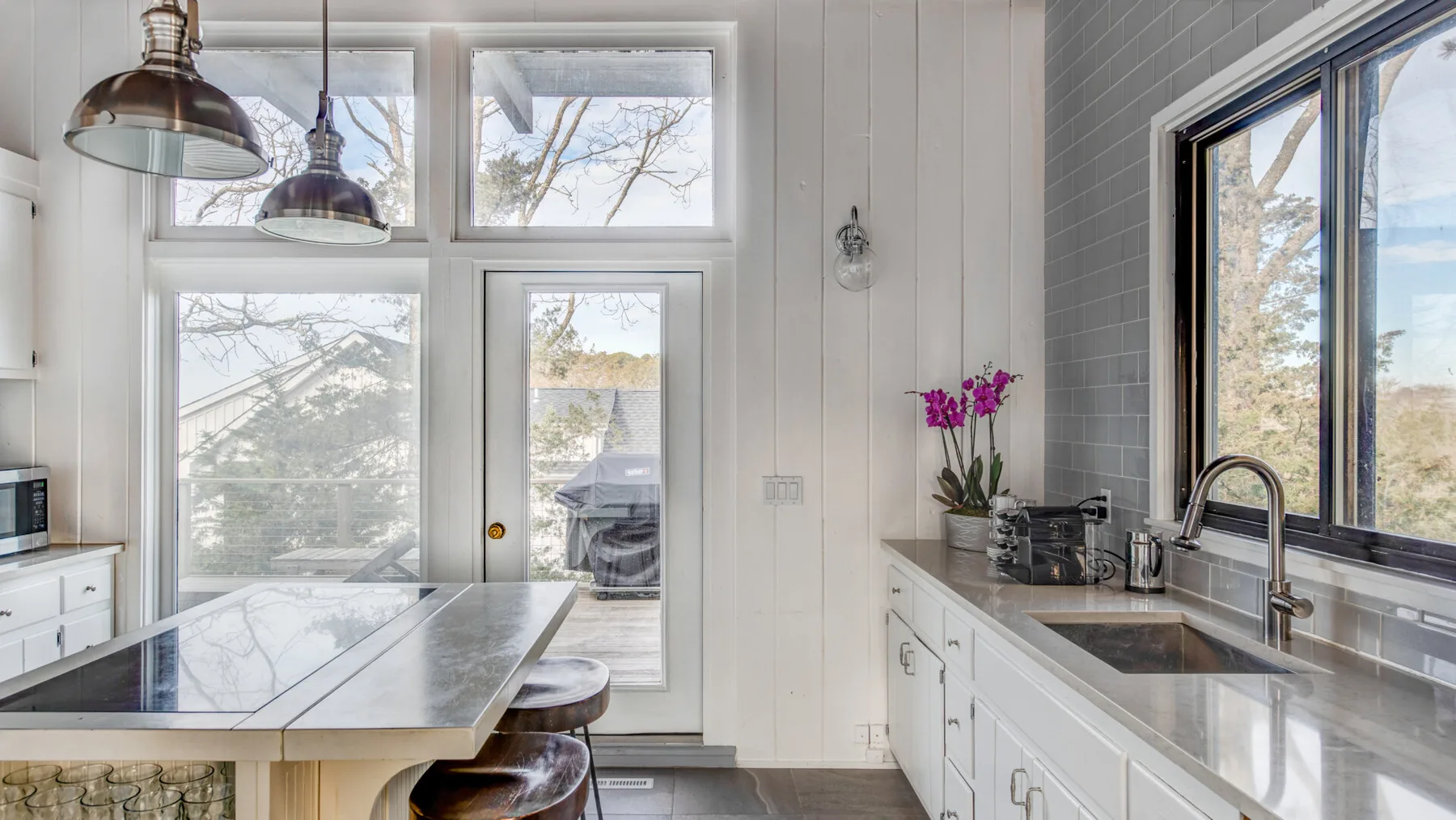 A bright kitchen with a central island, white cabinets, and large windows.